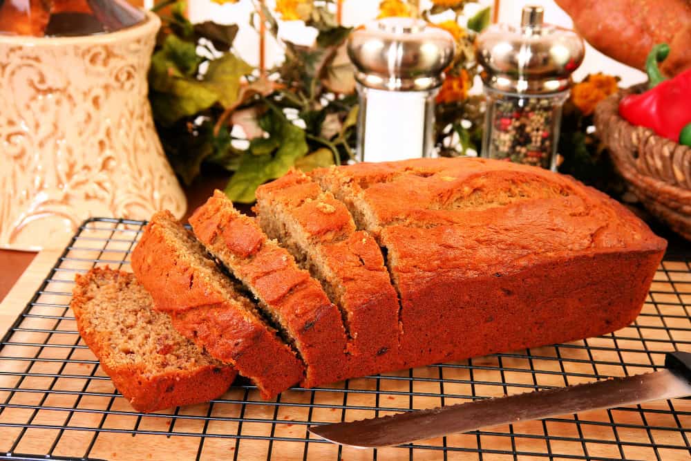 Loaf of Banana Bread, with some slices cut. cooling on a wire rack on kitchen counter