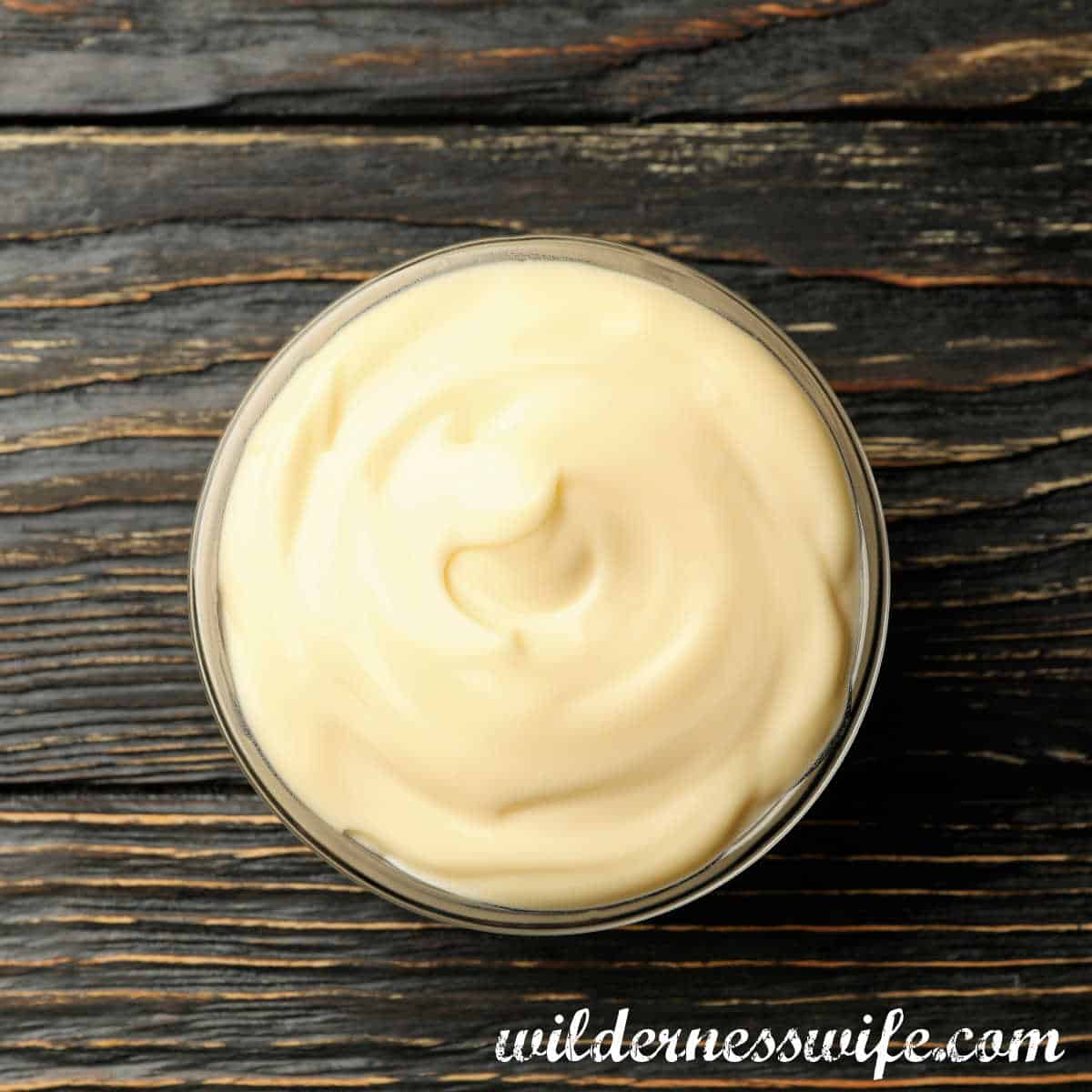 Glass Bowl of homemade mayonnaise set on a wooden table