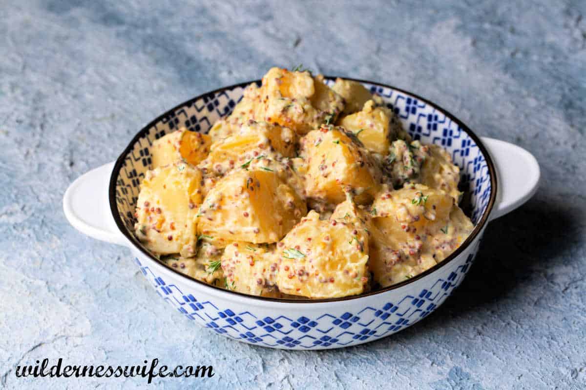 Potato salad in a blue and white bowl. The salad has been made with the KitchenAid Mayonnaise Recipe and is sitting on a light blue tablecloth.