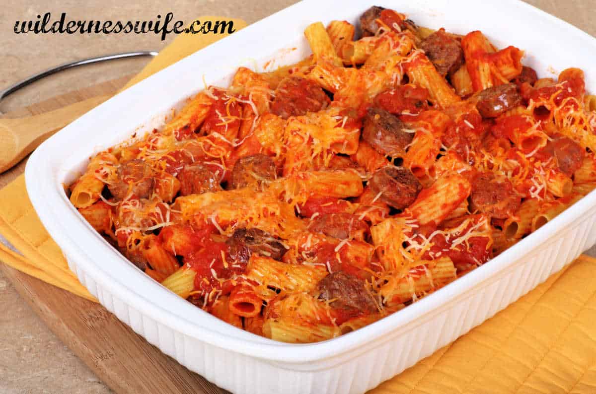White 9 x 13 serving dish filled with Italian sausage rigatoni set on wooden table
