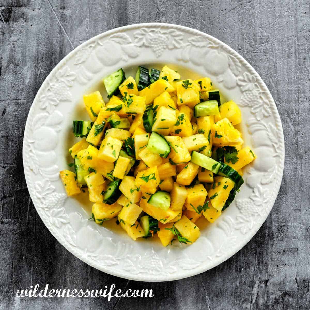White bowl filled with Pineapple Cumber Salad setting on grey wood table.