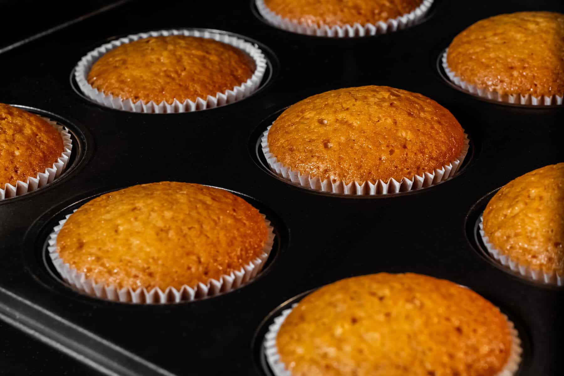 A pan of golden KitchenAid orange muffins with white paper wrappers showing.