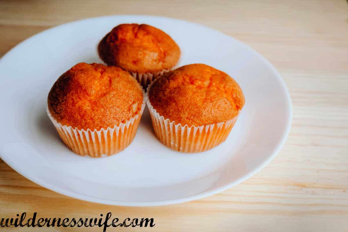 Three KitchenAid Orange Muffins on a white plate set on a blonde wood table